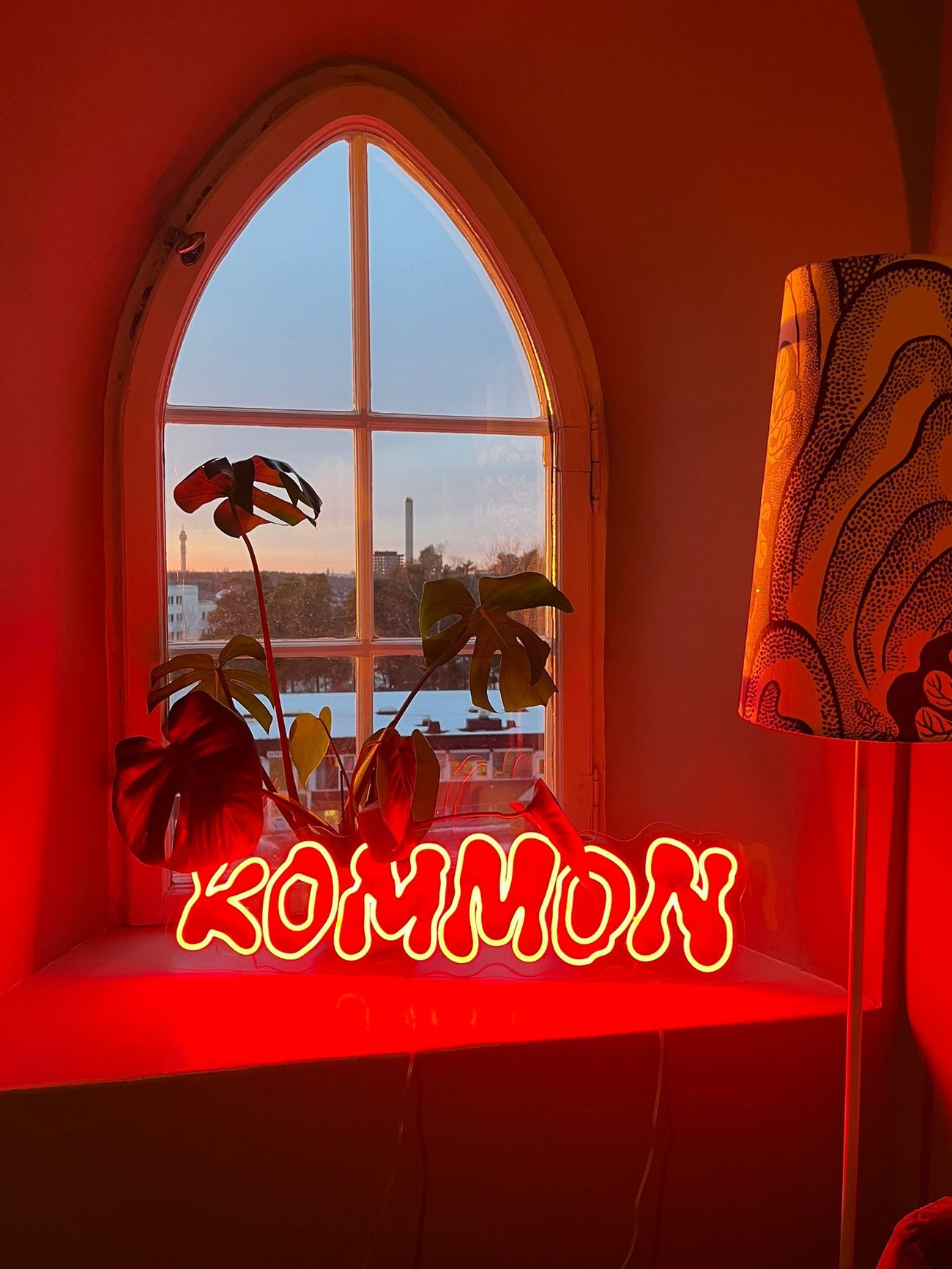 A red KOMMON neon sign in a curved window at dusk