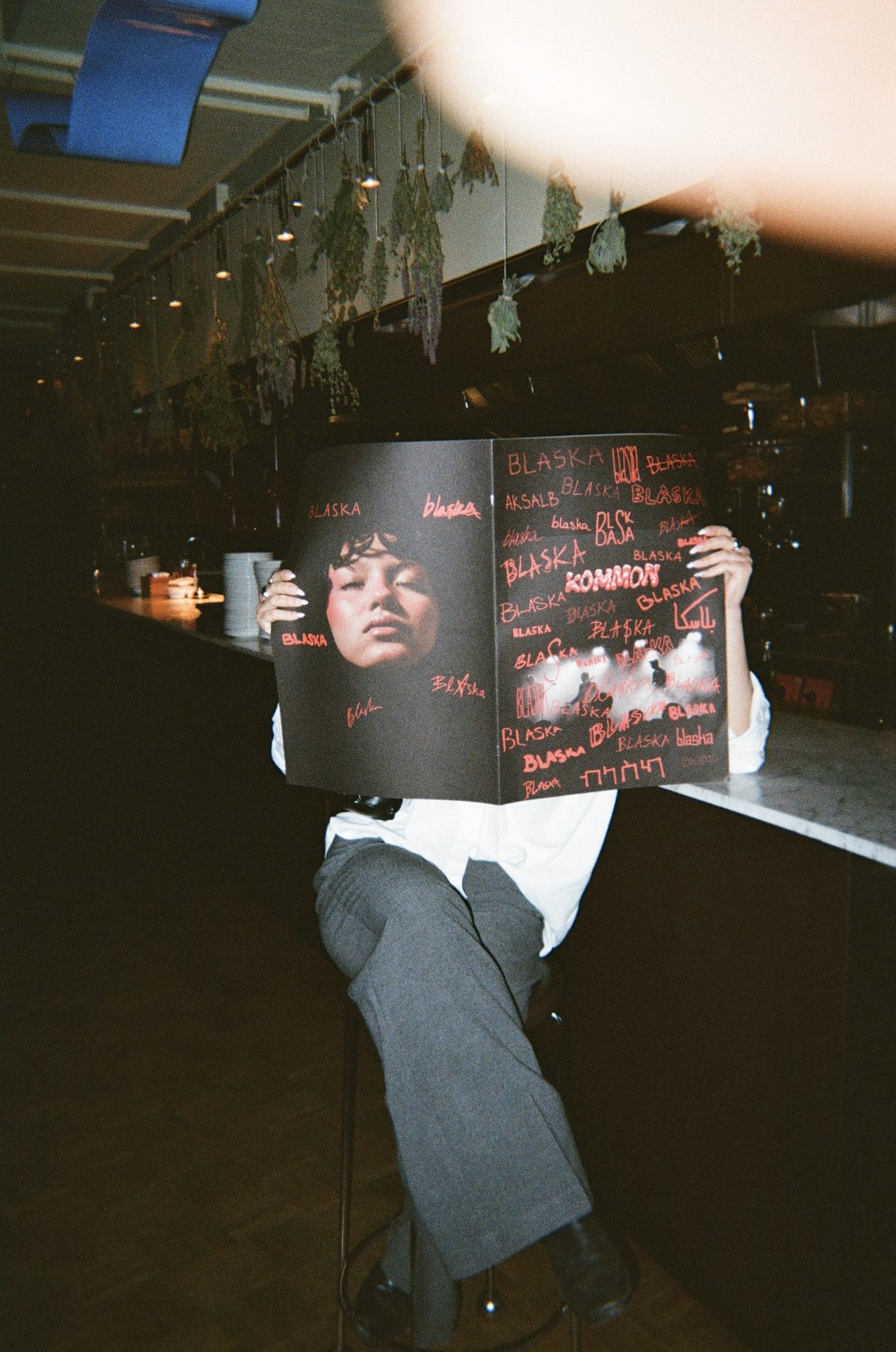 A person sits at a bar counter flipping through Blaska, the scrawl-covered cover facing out